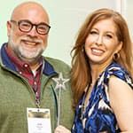 Two people smiling at the camera; the person on the left holds a star-shaped wand and wears a name badge.